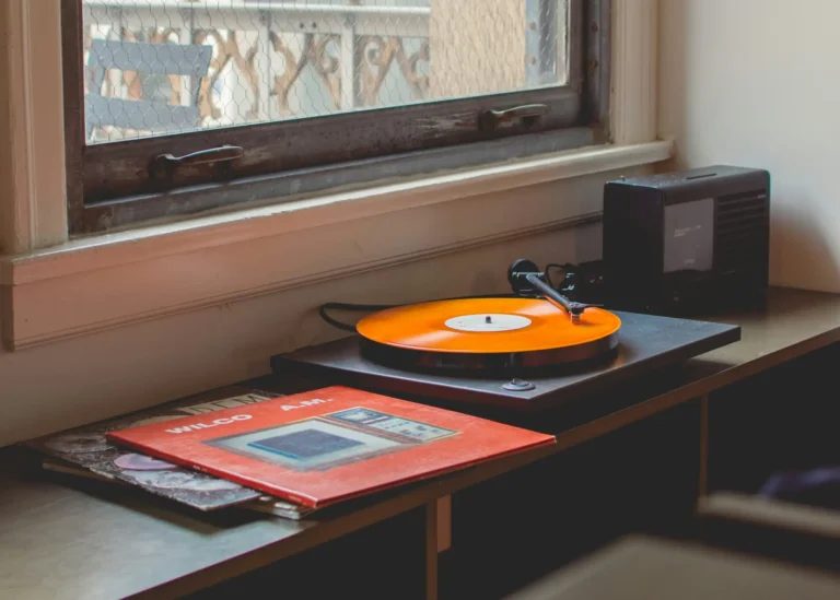 Platine vinyle pour débutant posée près d'une fenêtre avec vinyle orange en lecture et pochettes d'albums