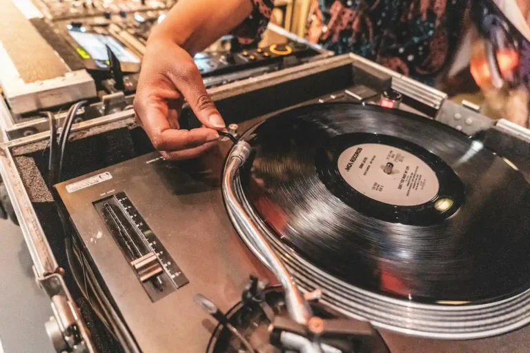Platine vinyle DJ en action dans un club avec vinyle en lecture et main du DJ sur le bras de lecture